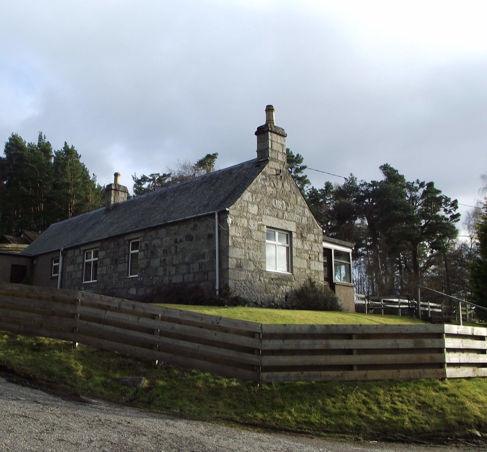 A granite cottage behind a timber fence with open garden ground at Nethy Bridge